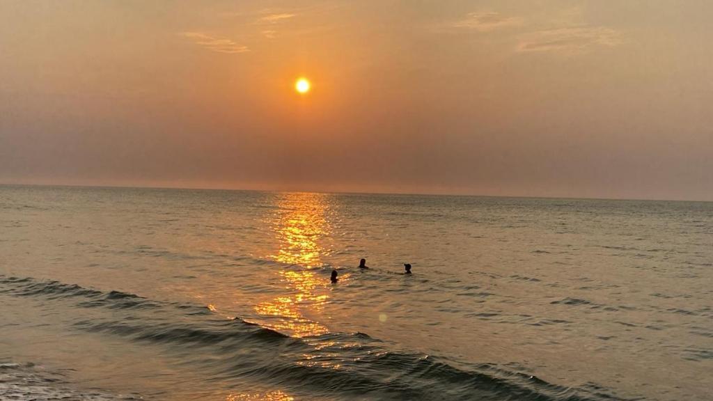 três pessoas nadando no oceano ao pôr do sol em Tu descanso ideal en santa Marta em Gaira