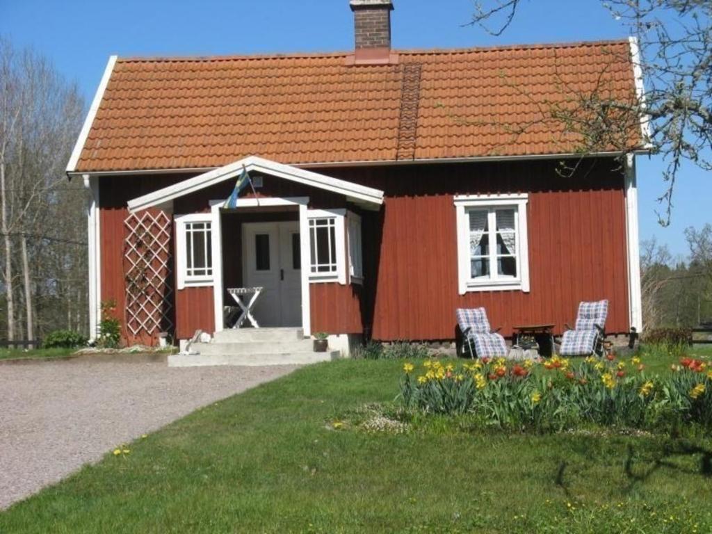 una casa roja con dos sillas delante en Idyllisches Bauernhaus in Småland, en Kättilstorp
