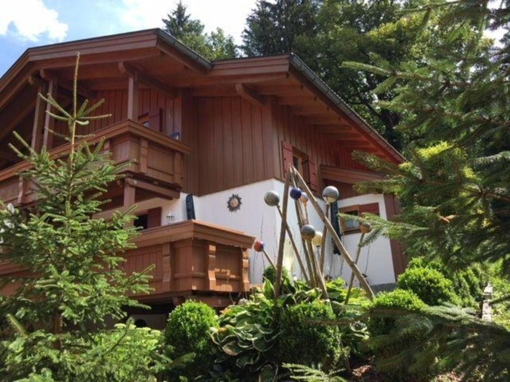 uma casa de madeira com árvores em frente em Ferienhaus in ruhiger Lage, mit Balkon, Terrasse und eigenem Gartenteil em Aschau im Chiemgau