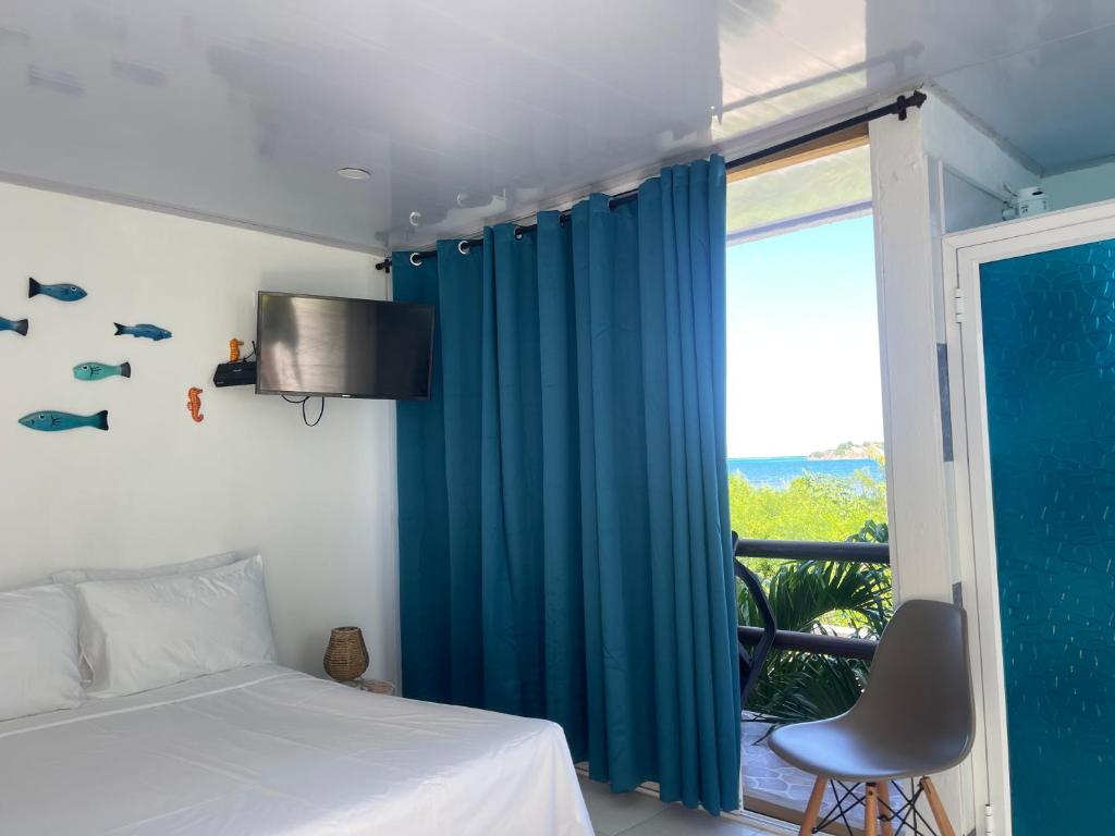 a bedroom with a bed and a window with blue curtains at Posada Sunrise View in Providencia