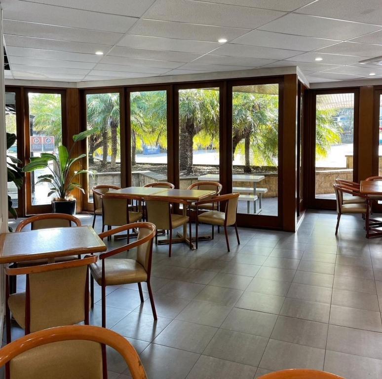 un comedor con mesas, sillas y ventanas en Time and Tide Hotel Motel, en Collaroy