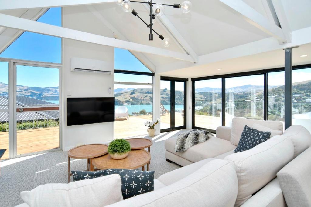 una sala de estar con muebles blancos y ventanas grandes. en Akaroa Harbour View - Christchurch Holiday Homes, en Akaroa
