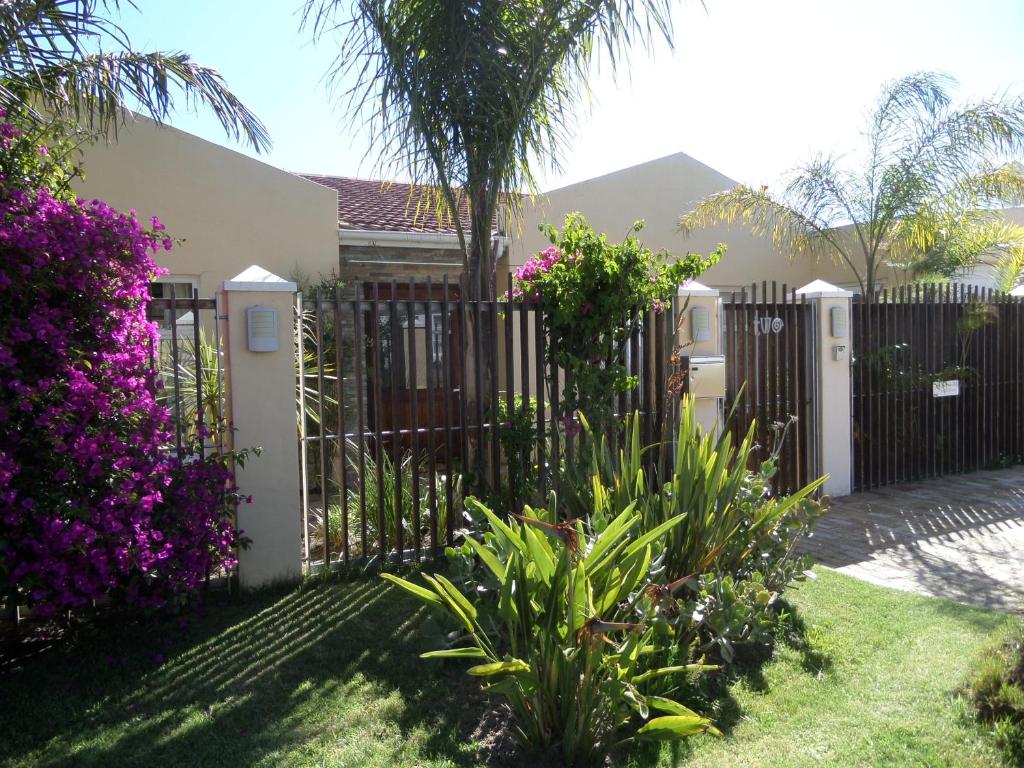 uma cerca em frente a uma casa com flores roxas em Kasa Nama em Edgemead