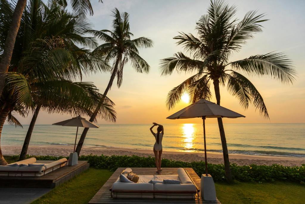 ホアヒンにあるCape Nidhra Hotelの夕日を眺めながら浜辺に立つ女