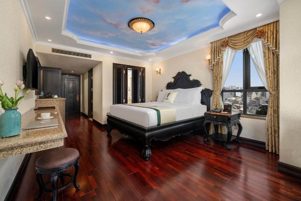 A spacious-looking bedroom with a carved bed, desk, minibar counter and urban window view.
