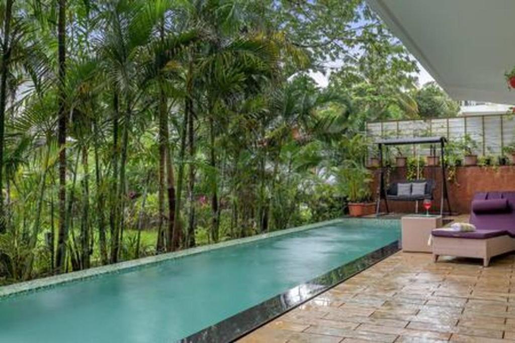 a swimming pool with palm trees in a backyard at sohonos · Luxurious 3bhk villa in Candolim in Goa