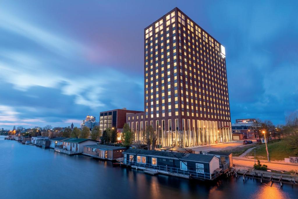 ein hohes Gebäude neben einem Fluss mit einem Gebäude in der Unterkunft Leonardo Royal Hotel Amsterdam in Amsterdam
