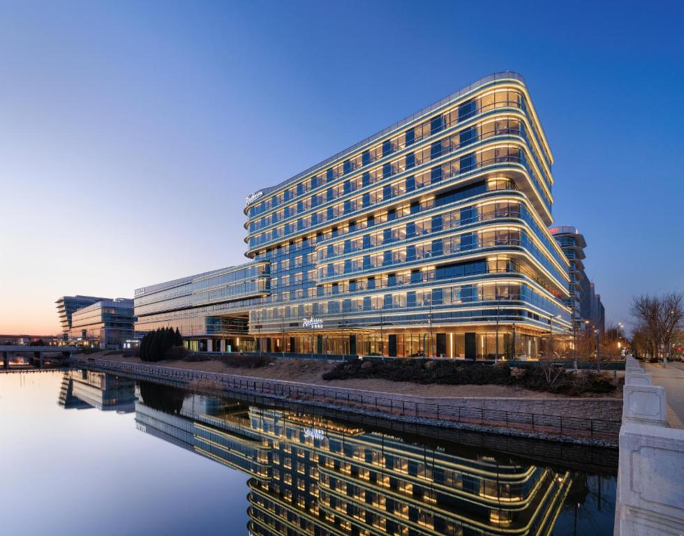 a large office building with a reflection in the water at Radisson Hotel, Beijing DaXing Airport in Beijing
