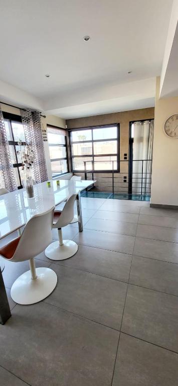 Cette grande chambre comprend des tables et des chaises blanches ainsi que des fenêtres. dans l'établissement Villa Camarguaise entre Plage et centre ville avec bassin extérieur, au Grau-du-Roi