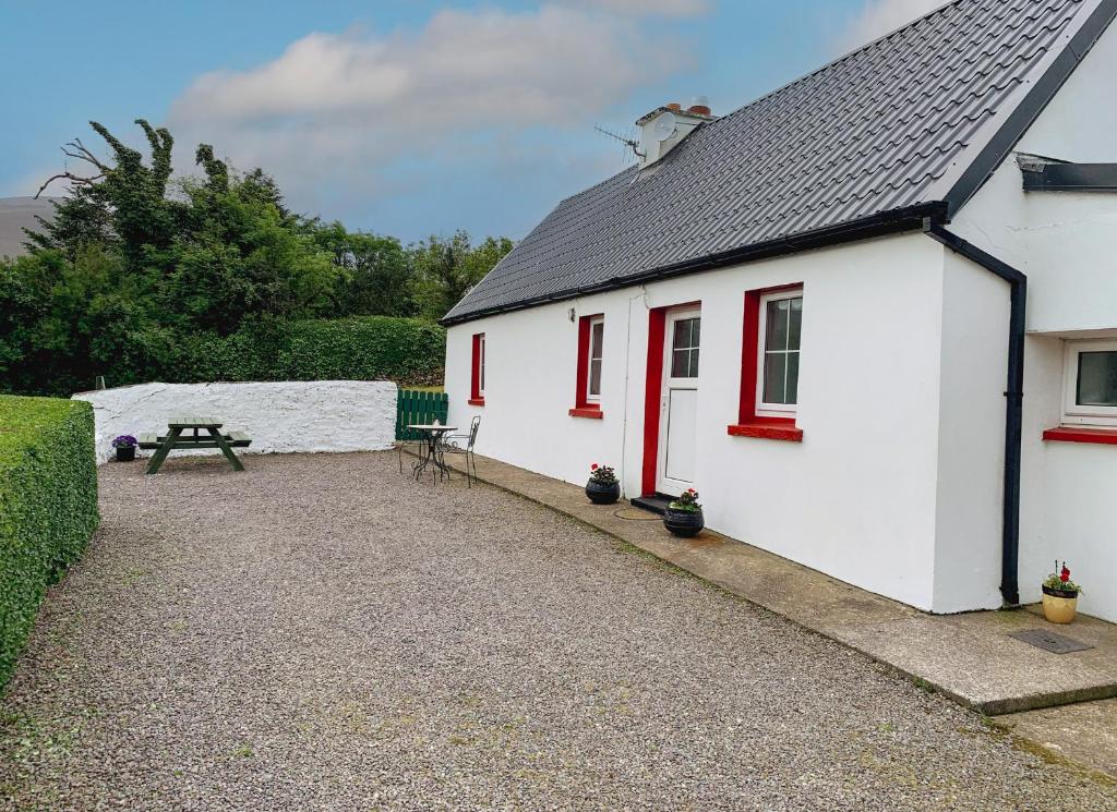 een wit huis met rode ramen en een picknicktafel bij Glenbeigh Holiday Cottage - Tigin Mamo in Glenbeigh