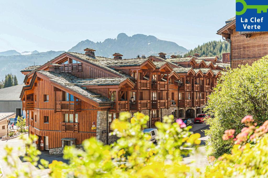a large wooden building with mountains in the background at Résidence Pierre & Vacances Premium Les Chalets du Forum in Courchevel