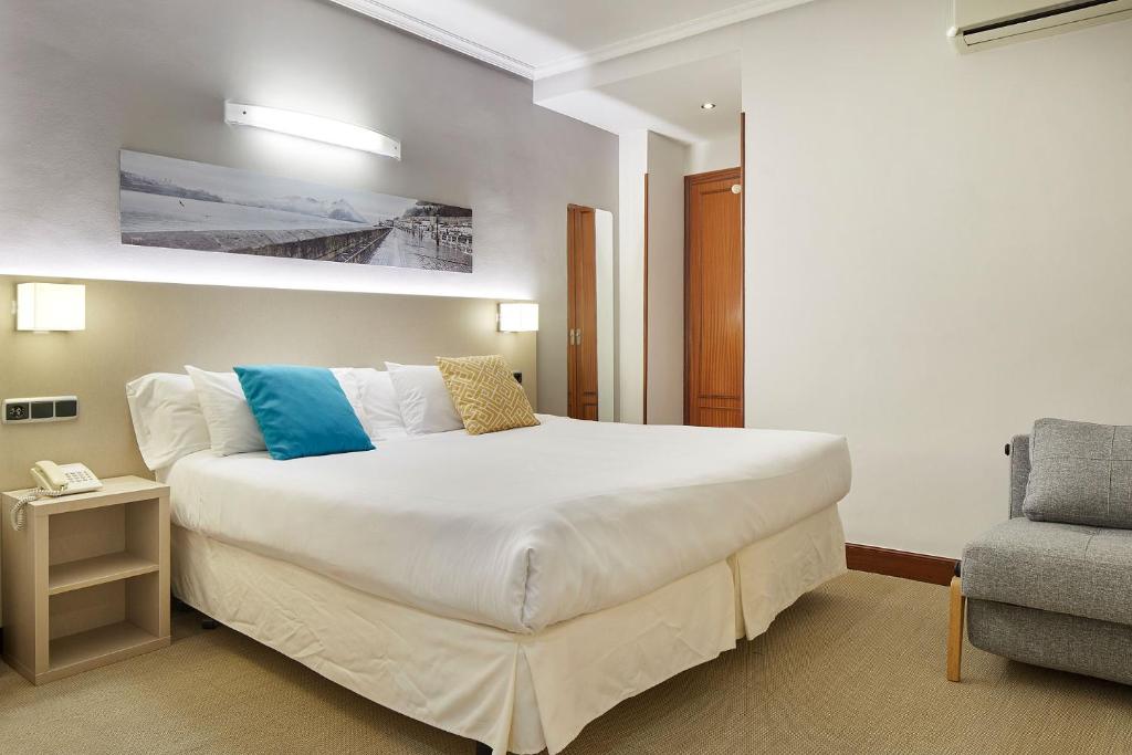 a bedroom with a large white bed and a chair at Hotel Parma in San Sebastián