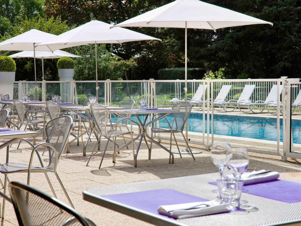 een groep tafels met stoelen en parasols naast een zwembad bij Novotel Marne-la-Vallée Noisy-le-Grand in Noisy-le-Grand