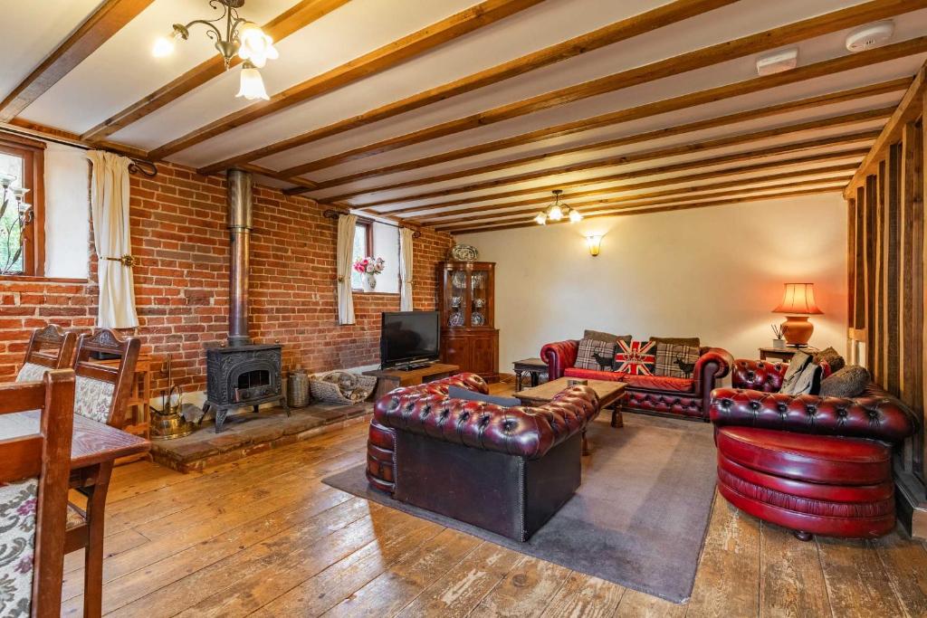 a living room with leather furniture and a brick wall at Threshers Barn and Shire Horse Barn in Cawston