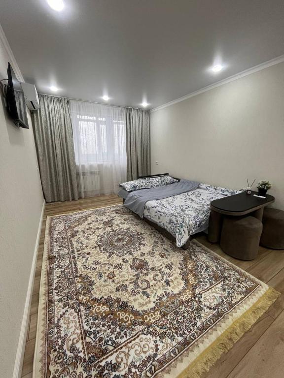 Schlafzimmer mit einem Bett, einem Tisch und einem Teppich in der Unterkunft Квартира in Sätbaev