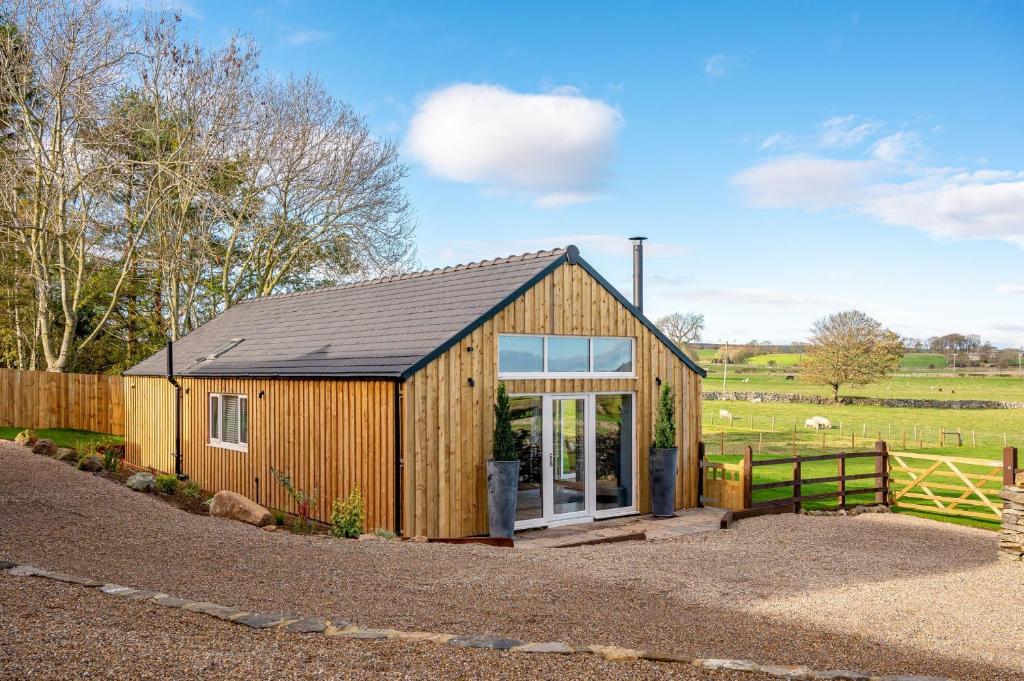 a small wooden building with a fence and a field at Bearskin Cottage in Leyburn