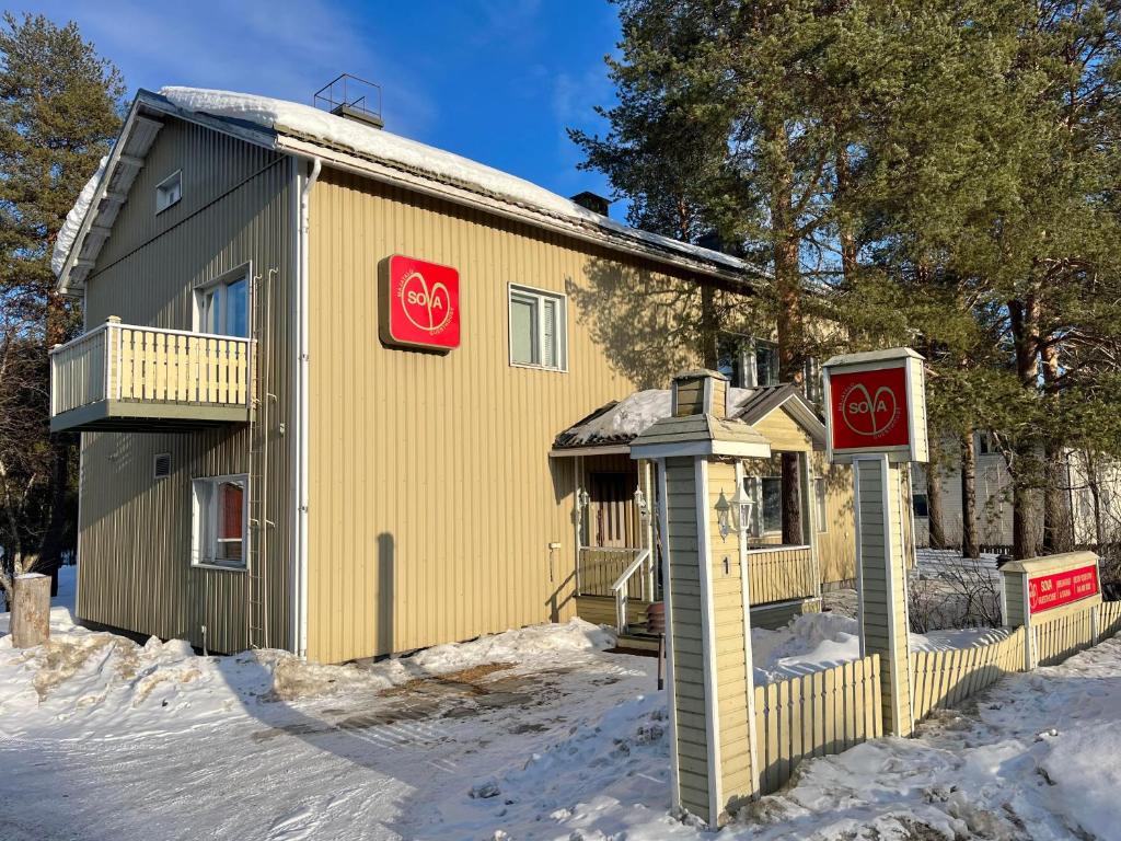 a yellow building with two signs on it in the snow at Sova Guesthouse in Sodankylä