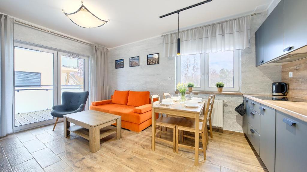 a kitchen and dining room with an orange couch and a table at Apartamenty Sun & Snow Szafirowa in Mielno