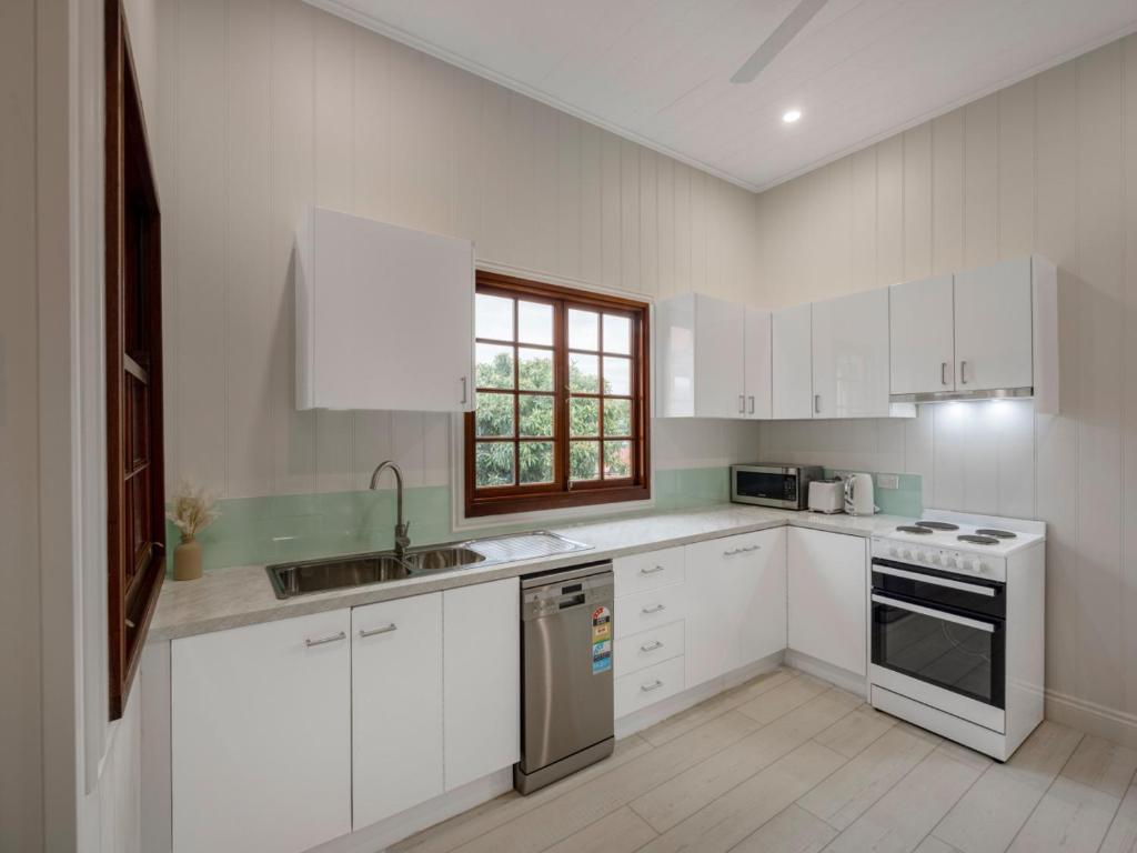 Una cocina con gabinetes blancos y un fregadero y una ventana. en Charming 3BR Inner City Haven Highgate Hill, en Brisbane