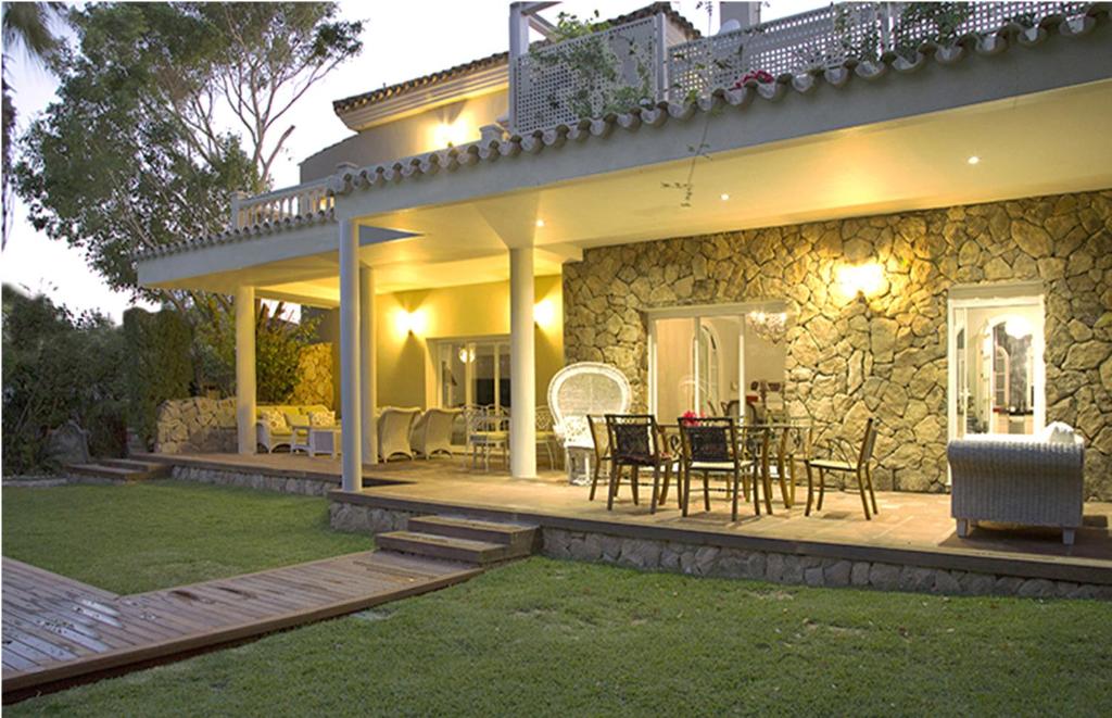 Cette maison dispose d'une terrasse avec une table et des chaises. dans l'établissement Villa de Lujo con Jardines y Piscina, à El Puerto de Santa María