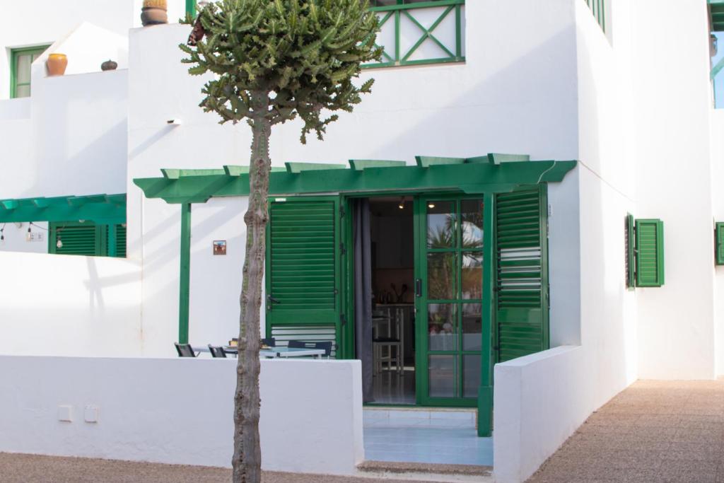 a tree in front of a white building with green shutters at CASA PAZ - COZY 2 BEDROOM APARTMENT CLOSE TO DORADA BEACH in Playa Blanca