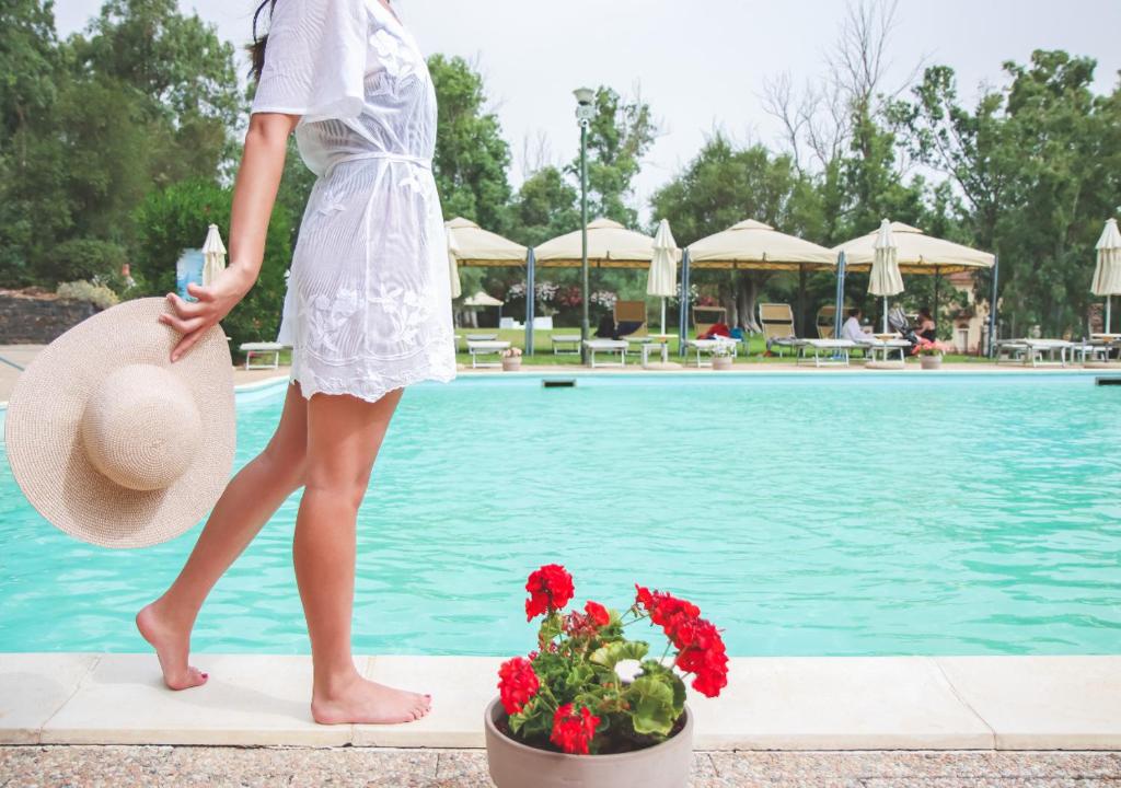 una mujer con un vestido blanco y un sombrero junto a una piscina en Antiche Terme di Sardara, en Sardara