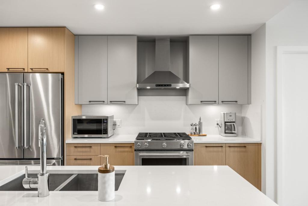 una cocina con armarios blancos y electrodomésticos de acero inoxidable en Modern 1000sqft+ Condo in Sidney, Ocean Views, Parking. Walk to Shops, Restaurants!, en Sidney