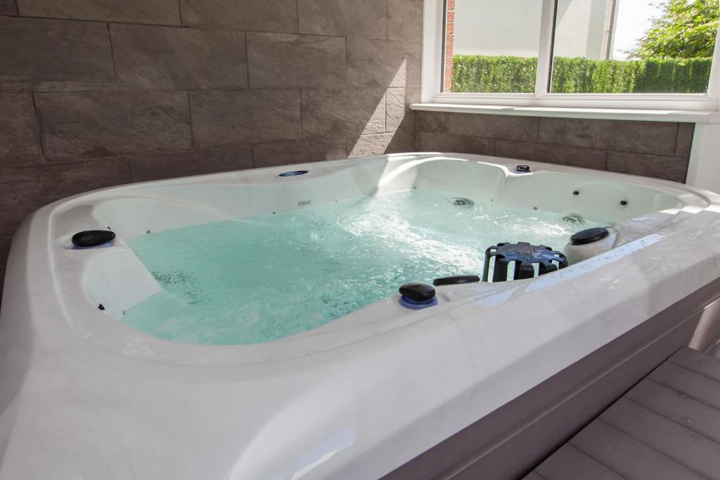 baño con bañera blanca y ventana en Luxe Arthurs Seat View Townhouse with Hot Tub, en Edimburgo