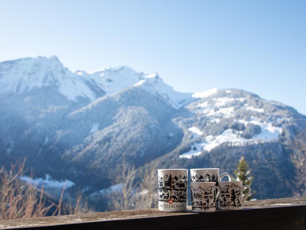 vier Kaffeetassen auf einem Felsvorsprung mit Bergen in der Unterkunft Apartment Les Chavonnes by Interhome in Gryon