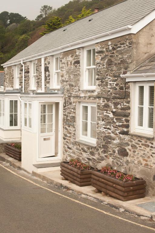 a stone house with white doors and flowers on a street at Cottages at the Lugger in Portloe