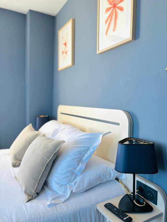 a blue bedroom with a bed with a lamp and pillows at Hôtel De La Marine in Arromanches-les-Bains