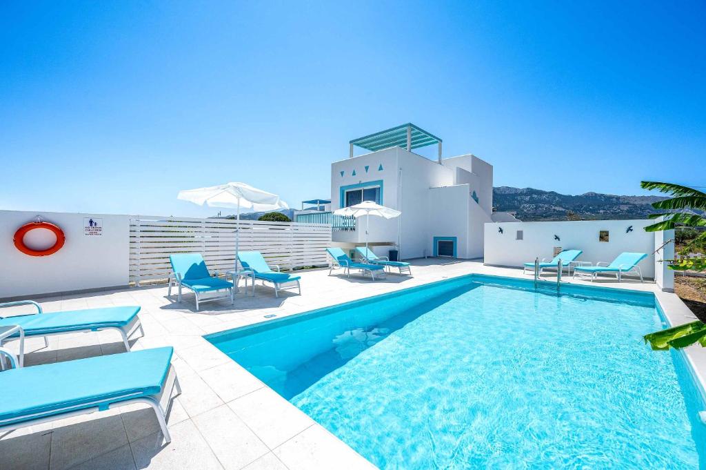 a swimming pool with blue chairs and a house at Villa Xenos Ciel in Tigaki