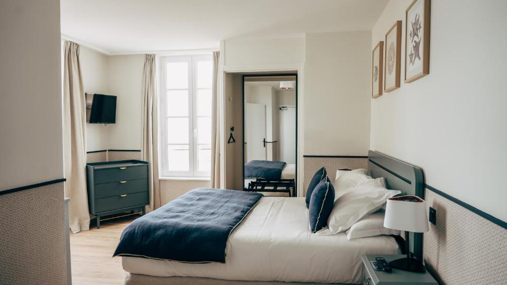 a bedroom with a bed and a dresser and a mirror at Hôtel De La Marine in Arromanches-les-Bains