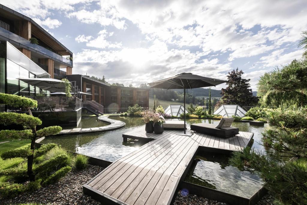 une terrasse en bois avec un parasol et un étang dans l'établissement Alpine Spa Resort Viktoria, à Avelengo