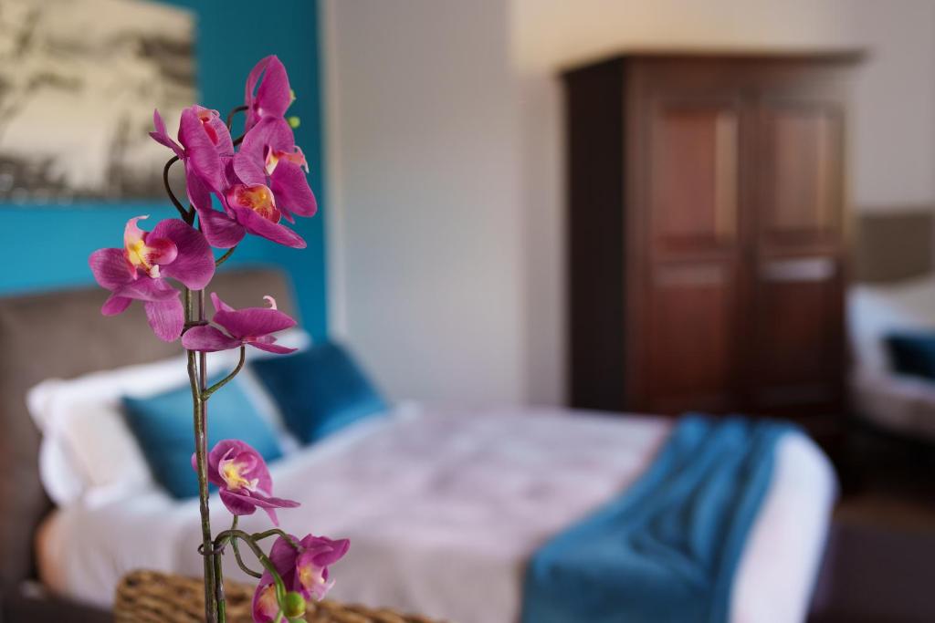 un jarrón con flores púrpuras delante de una cama en La Dolce Vita, en Regalbuto