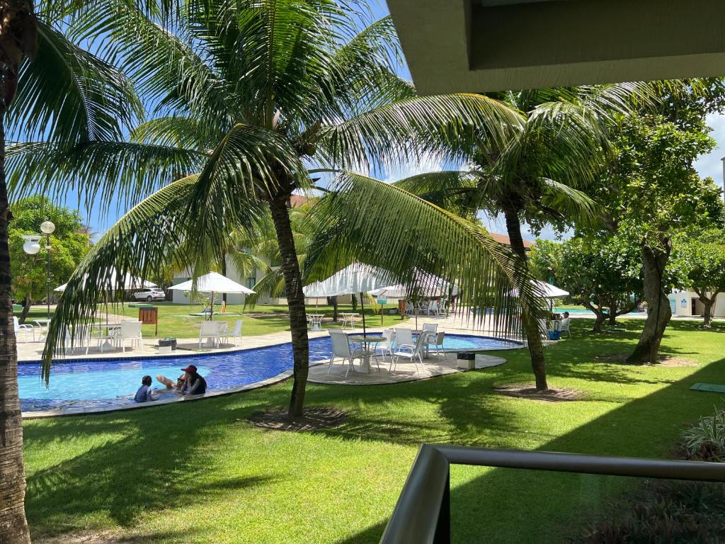una piscina con palmeras y gente sentada en ella en Carneiros Beach Resort - Flat 111-D en Praia dos Carneiros