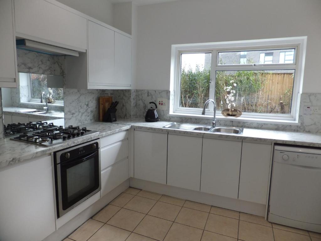 a kitchen with white cabinets and a sink and a window at 15 mins from East Croydon to Central London, Gatwick - Sleeps up to 7 couples plus Babies - Free WiFi, Parking - Next to Lloyd Park, Great for Walkers - Ideal for Contractors - Families - Relocators in Croydon