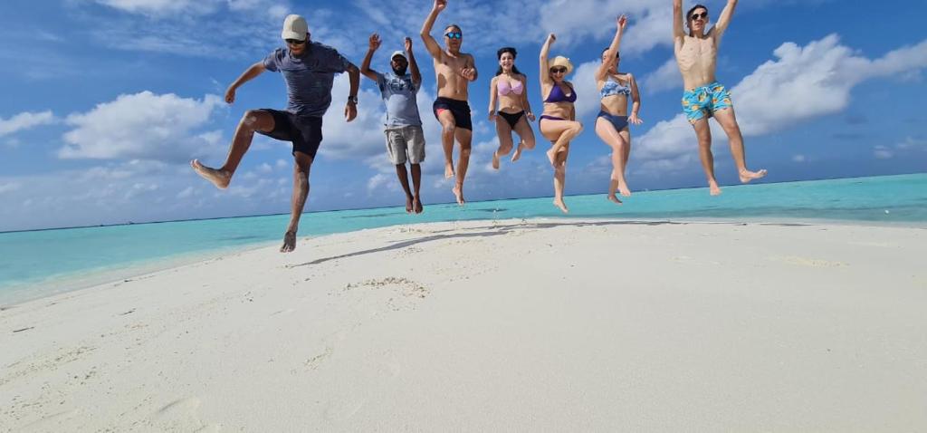 a group of people jumping in the air on a beach at Liberty Guesthouse Maldives in Mahibadhoo