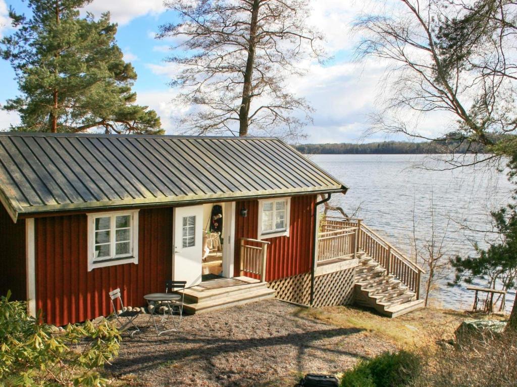 a small red house with a deck and water at Holiday home FäRENTUNA in Kungsberga