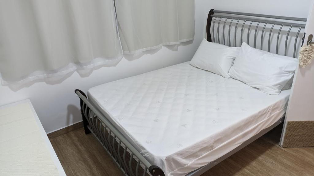 Cama pequeña con sábanas y almohadas blancas en Charmoso e confortável com A/C, en Pindamonhangaba