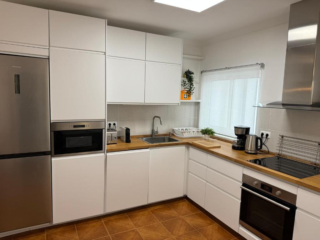 una cocina con armarios blancos y electrodomésticos de acero inoxidable en Cabo Sardão Guest House, en Odemira