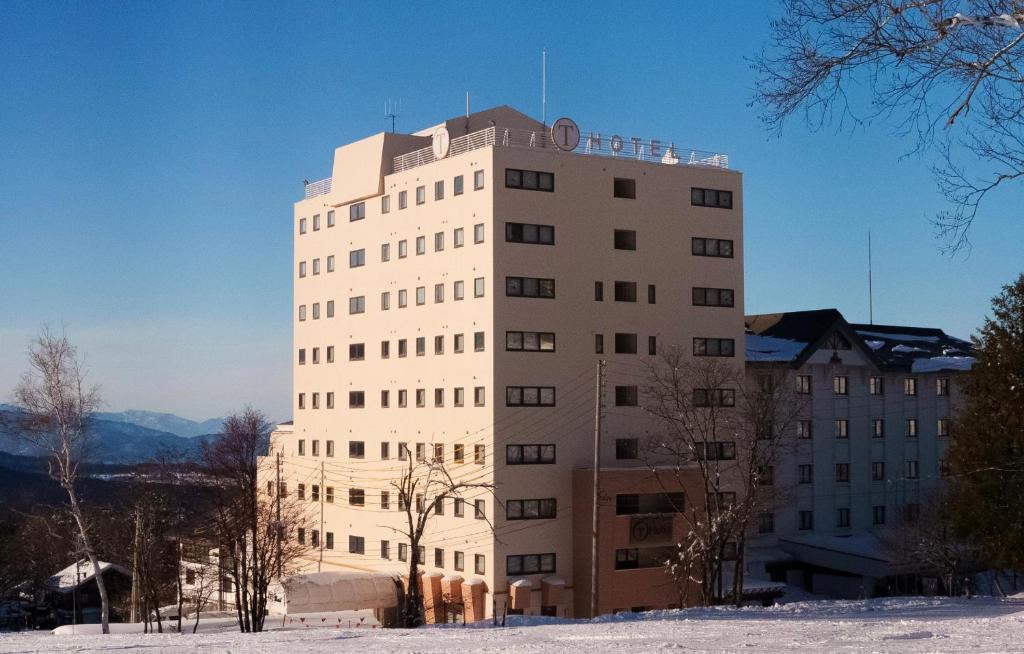 um edifício branco alto com neve no chão em T Hotel Ryuoo em Shimotakai