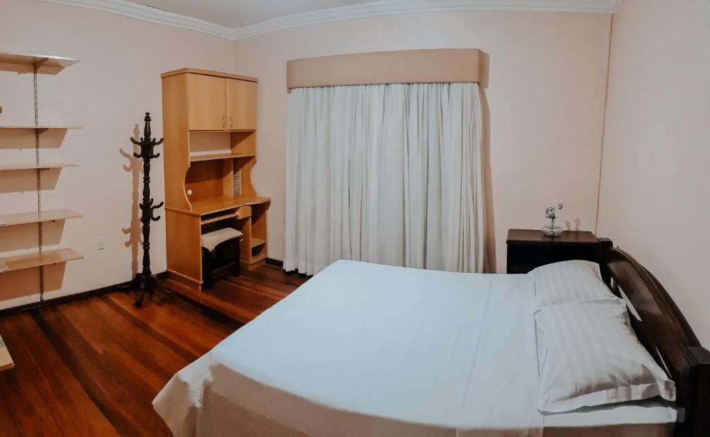 a bedroom with a bed and a desk and a window at Quarto Aconchegante na - Peniel Guesthouse in Gramado