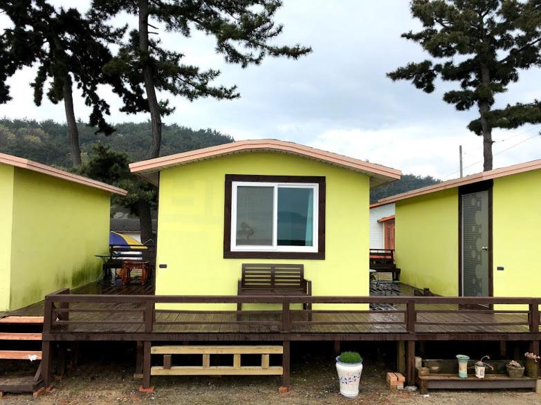 uma pequena casa amarela com um grande deque de madeira em 바다와정원 Sea and Garden em Boryeong
