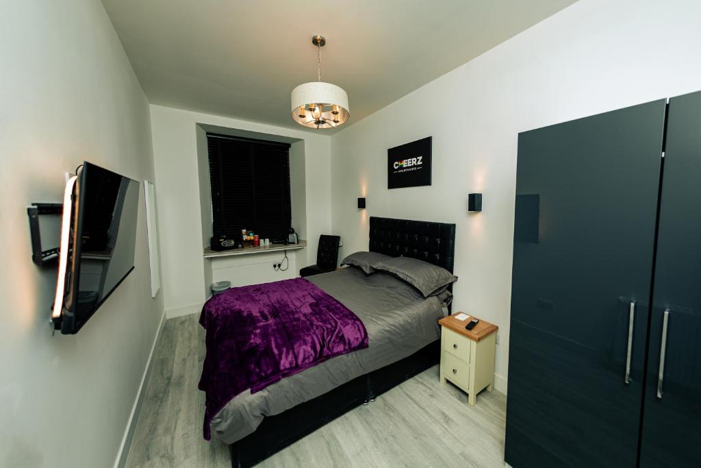 a bedroom with a bed with a purple blanket and a tv at CHEERZ Apartments in Aberdeen
