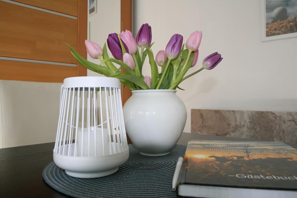 Un jarrón blanco con tulipanes púrpuras junto a un libro. en Abschalten und Urlaub machen im Herzen der Rhön, en Münnerstadt
