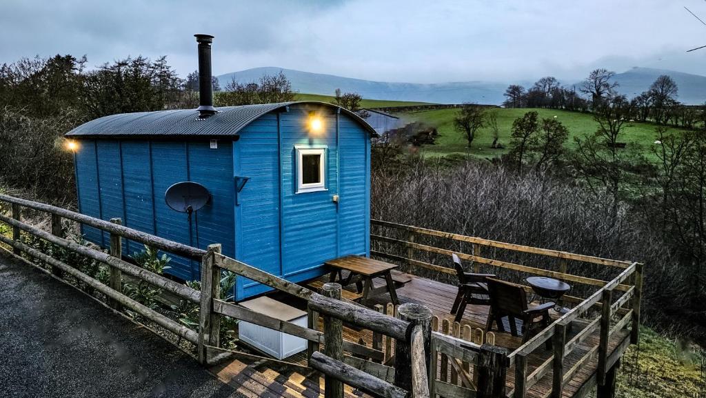 a blue shed with a table and chairs on a deck at Cuckoo at Wild Valley Huts in Oswestry