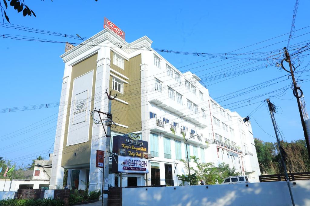 een hoog wit gebouw met een bord ervoor bij RAS Hotels in Kumbakonam