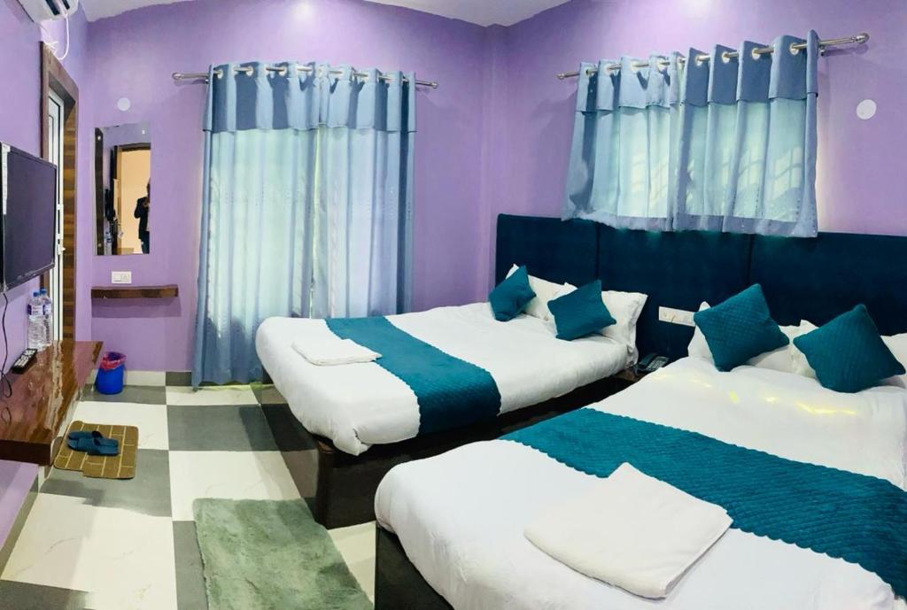 2 Betten in einem Zimmer mit lila Wänden und blauen Vorhängen in der Unterkunft Hotel Mangalam in Siddharthanagar