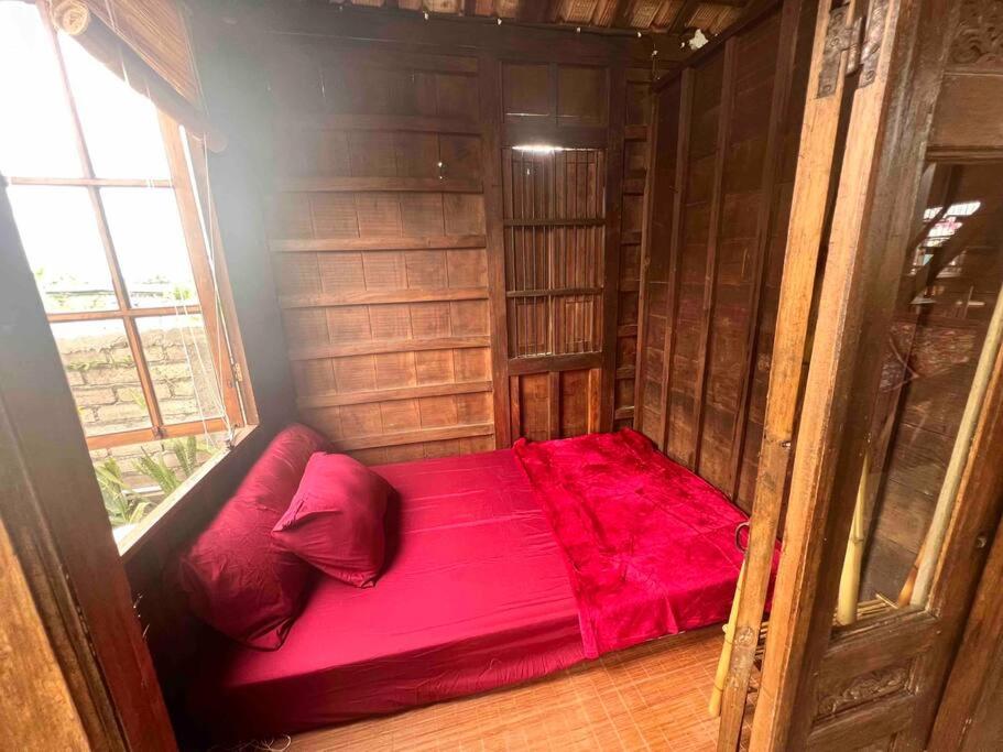 a red bed in a small room with a window at Di Kubu YR in Jembrana